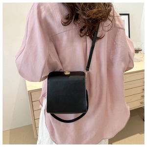 Détail d'un sac bandoulière carré en cuir noir avec un fermoir doré sur un mannequin
