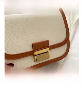 Detail of canvas and brown leather stitching with a gold metallic buckle on a flap bag