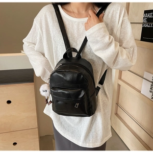 Detail of black patchwork backpack with silver hardware and a white plush keychain