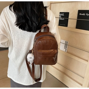 Brown patchwork leather backpack with a white fluffy keychain charm on a model back
