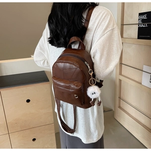 Détail d'un mini sac à dos en cuir marron avec charme en peluche porté par un mannequin