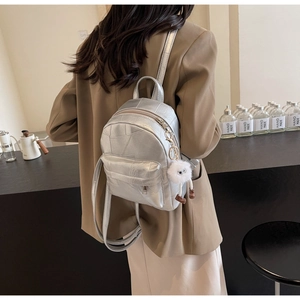 Détail du mini sac à dos argenté métallisé avec coutures et pompon blanc décoratif