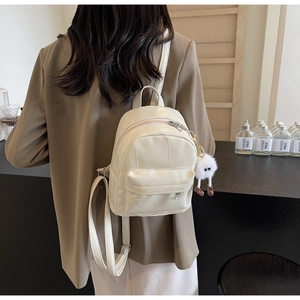 Détail d'un mini sac à dos blanc crème avec matelassage géométrique et breloque en peluche
