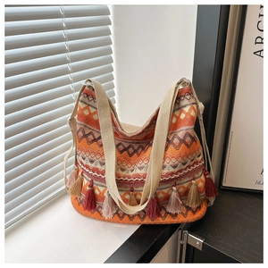 Detail of vibrant orange bohemian woven tote bag featuring ethnic tassels and wide strap