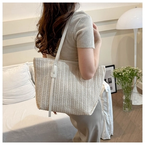 Close-up of fine woven straw texture and faux leather straps on a large summer tote bag