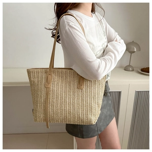 Close-up of woven beige straw tote bag texture with leather straps on model's shoulder
