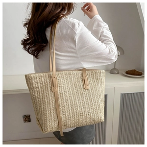 Model wearing a large ivory woven tote bag with brown leather straps in a home setting