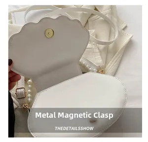 Dettaglio borsa bianca a conchiglia con chiusura magnetica dorata e tracolla di perle