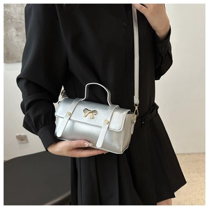 Detail of silver metallic mini bag featuring golden bow accent and crossbody strap