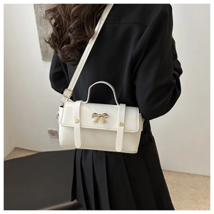 White leather crossbody bag with gold bow clasp shown on a model in a black blazer