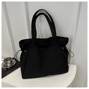 Detail of minimalist black tote bag with side drawstring on a white geometric stand