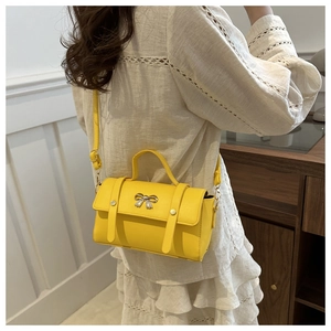 Detail of yellow crossbody bag with silver bow buckle worn over a white wavy top