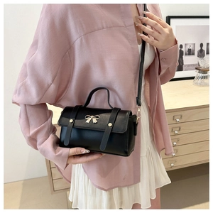Detail of black crossbody bag with golden bow hardware and rivet leather straps