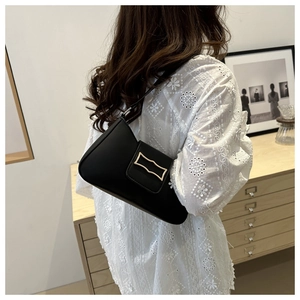 Detail of a black leather crescent underarm bag with gold buckle on a model in white lace
