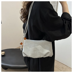 Détail du sac nuage gris clair montrant la texture suédée nacrée et le nœud perlé ambre
