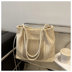 Detail of beige knit tote bag showing vertical woven texture and leather logo patch