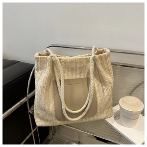 Detail of cream woven tote bag featuring rope handles and leather logo patch in a modern room