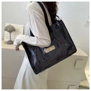 Close-up of a glossy black tote bag with a minimalist leather patch and gold lettering