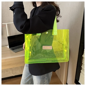 Detail of neon yellow transparent tote bag showing PVC material and branded leather patch