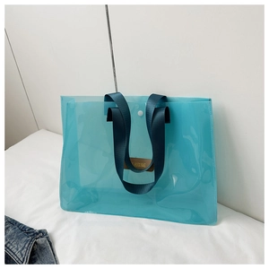 Detail of light blue transparent PVC tote bag with navy nylon handles and leather logo patch