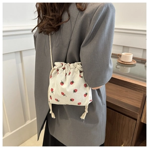 Detailed view of beige corduroy bucket bag with red strawberry print and drawstring closure