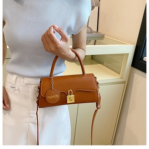 Detail of a brown leather shoulder bag featuring a golden square lock and fashion charm