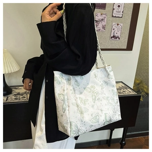 Detail of white tote bag with green butterfly print and woven straps on model