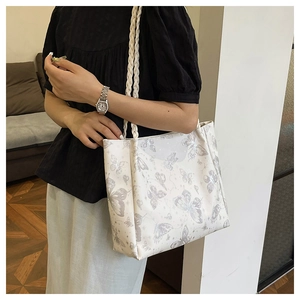 Close-up of a white tote bag featuring gray butterfly prints and woven rope handles