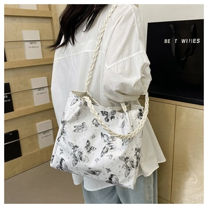 Detail of white tote bag featuring black butterfly prints and woven shoulder straps