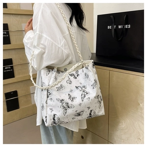 Detail of white tote bag featuring black butterfly print and braided shoulder straps
