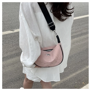 Outdoor shot of a pink crescent crossbody bag with adjustable wide black shoulder strap