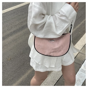 Pink crescent shoulder bag with black trim and silver buckle on casual white outfit