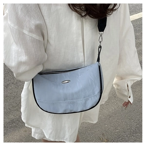 Outdoor shot of light blue nylon crescent bag with wide black shoulder strap on model
