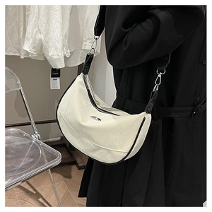 White hobo bag with black trim and wide strap styled on a model in a minimal setting