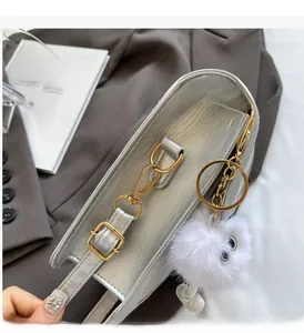 Detail of grey crossbody bag featuring glossy gold hardware and fluffy white charm