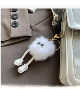 Close-up of white plush monster keychain with rope legs on a stylish handbag