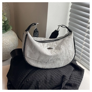 Close-up of metallic silver pleated texture and oval metal tag on half-moon shoulder bag