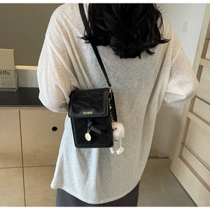 Close-up of a black pleated crossbody phone bag with a white plush doll charm