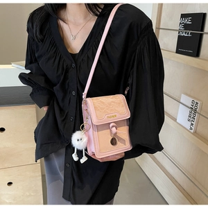 Close-up of pink crossbody bag with gold Fashion text and white plush monster charm