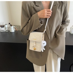 Close-up of cream mini crossbody bag with FASHION logo and plush charm detail