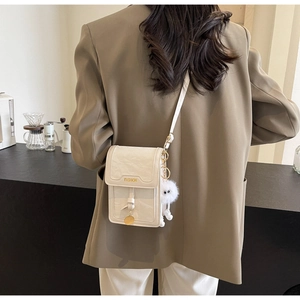 Close-up of beige crossbody phone bag with gold metal trim and plush charm detail