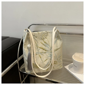 Detail of bamboo leaf embroidery on a light-colored canvas tote bag with silk tassel charm
