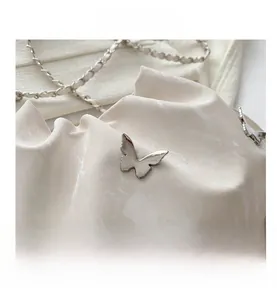 Macro detail of cream leather bucket bag with silver butterfly metal ornament and chain strap
