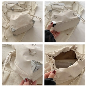 Detail view of cream drawstring bucket bag with silver metal corners and butterfly charm