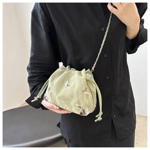Detail of light green bucket bag featuring silver butterfly charms and drawstring closure