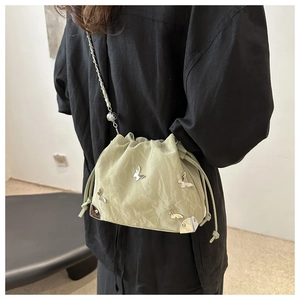 Light green drawstring bucket bag with silver butterfly details on a model shoulder
