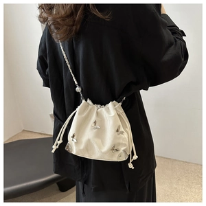 Detail of a white drawstring bucket bag with silver butterfly charms and chain strap