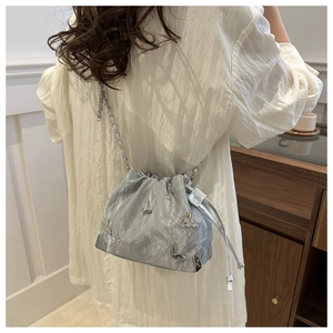 Detail of silver drawstring bucket bag with metal butterfly and chain strap