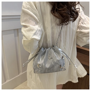 Detail of silver drawstring bucket bag with 3D metal butterflies and chain strap