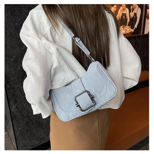 Detail of light blue textured shoulder bag with silver square buckle worn by model